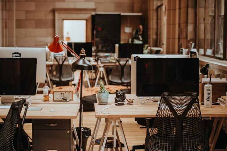 Oficina de coworking con un diseño industrial y acogedor en Spain, equipada con escritorios de madera, sillas ergonómicas, lámparas de escritorio, computadoras y decoración como plantas y figuras. El ambiente es cálido, con iluminación tenue y paredes de piedra, creando un espacio de trabajo inspirador y colaborativo.