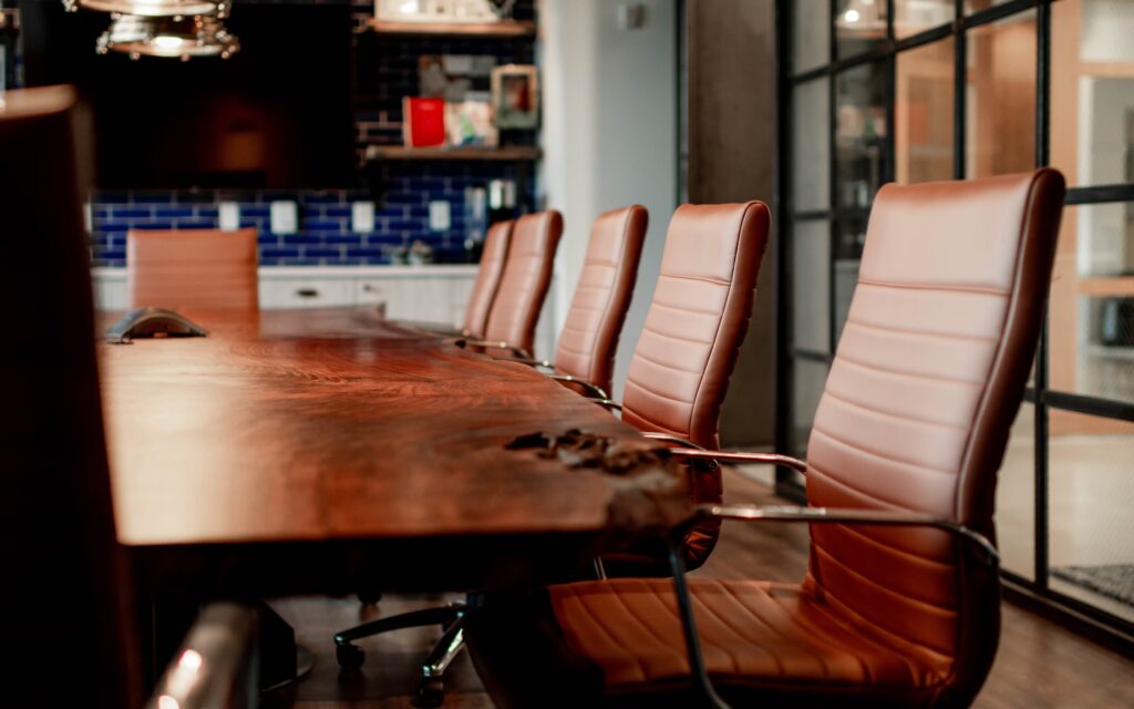 Sillas de cuero marrón alrededor de una mesa de madera natural en una sala de conferencias con decoración moderna y acogedora.